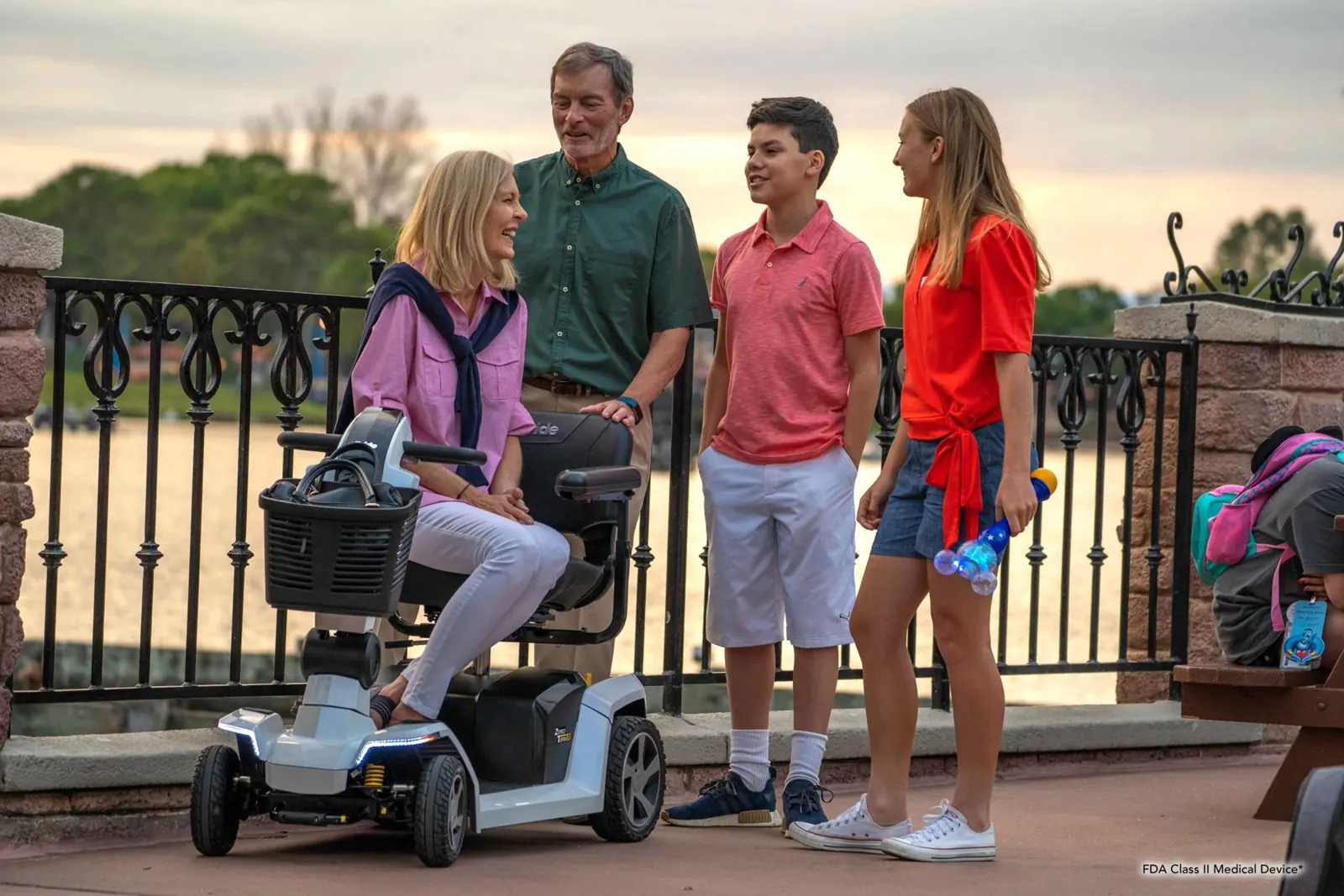 A woman seated on a mobility scooter talking with family beside a riverside railing