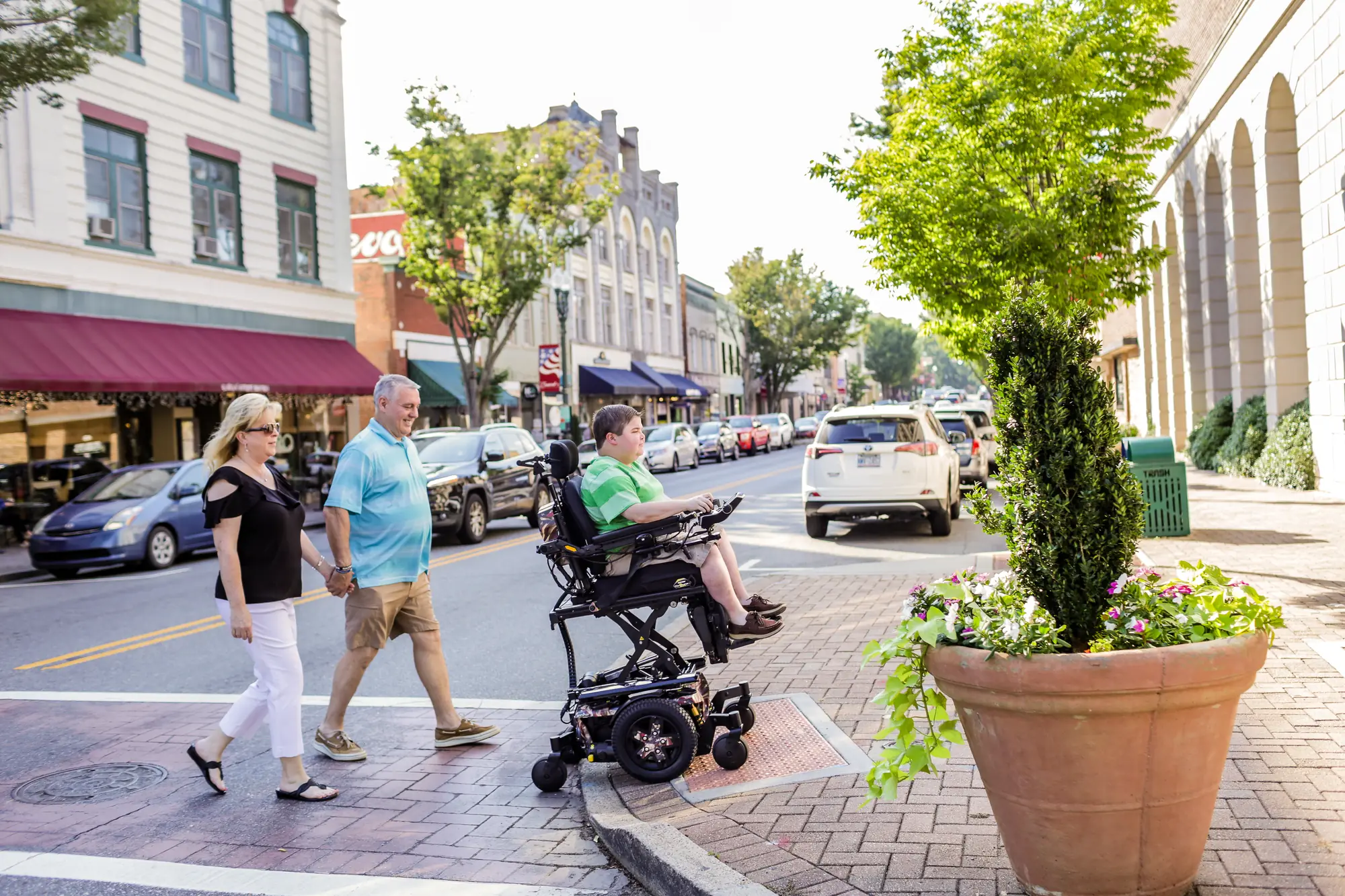 A young man in a power wheelchair crossing a town street with his parents