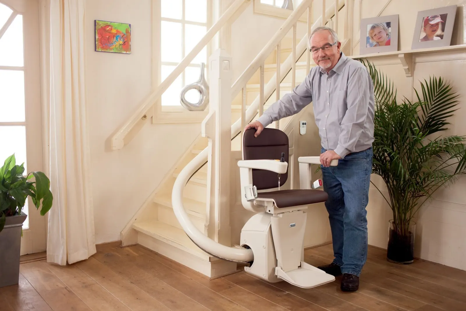 A man standing beside a seated stairlift at the bottom of his home staircase
