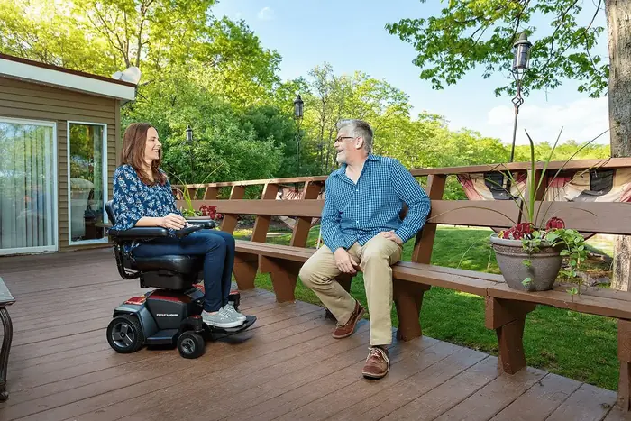 A woman in a power wheelchair chatting with a friend on a backyard deck