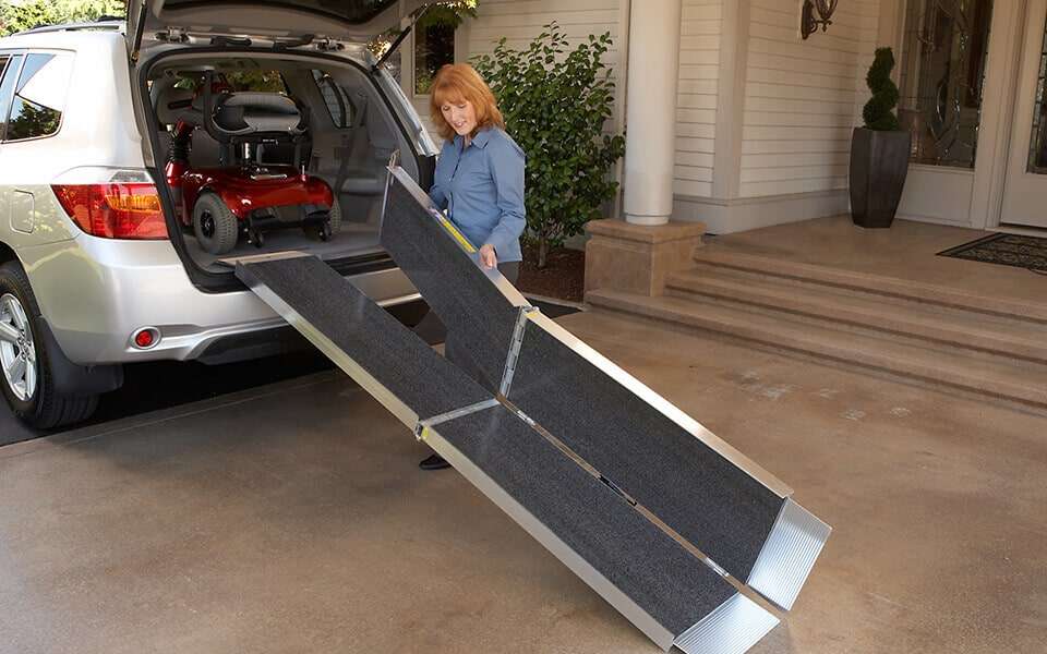 Woman loading a red scooter into a silver SUV using the trifold ramp