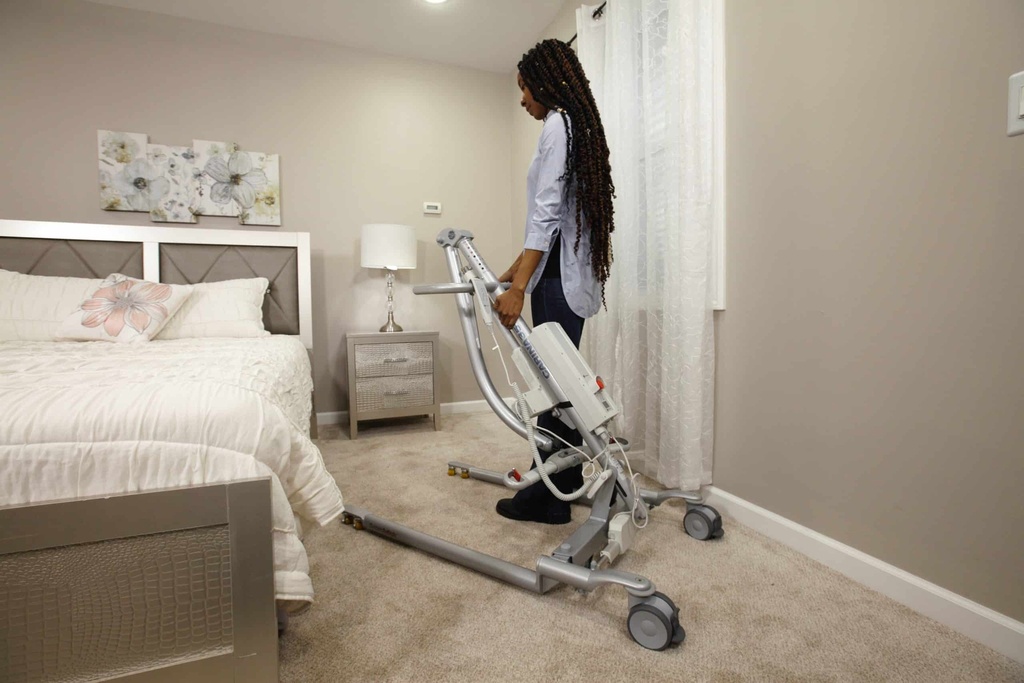 A carer wheeling the Carina 350 lift past a bed in a bedroom