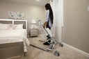 A carer wheeling the Carina 350 lift past a bed in a bedroom