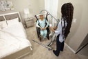 A person in a wheelchair wearing a sling on the Carina 350, with a carer at the controls