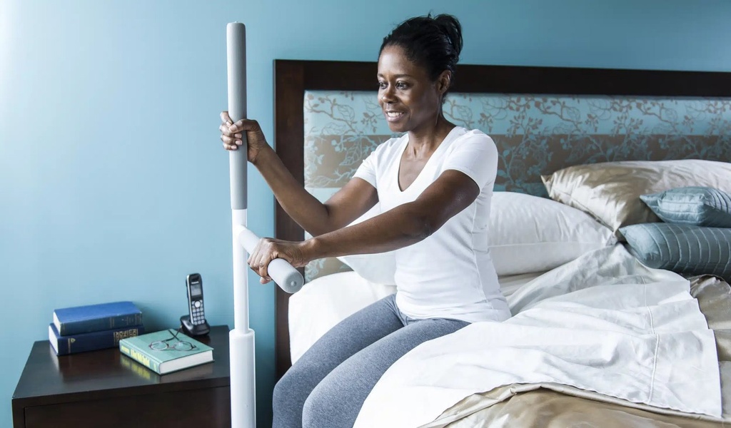 Woman on the edge of her bed holding the upright grip and the swing bar to stand up