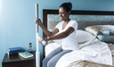 Woman on the edge of her bed holding the upright grip and the swing bar to stand up