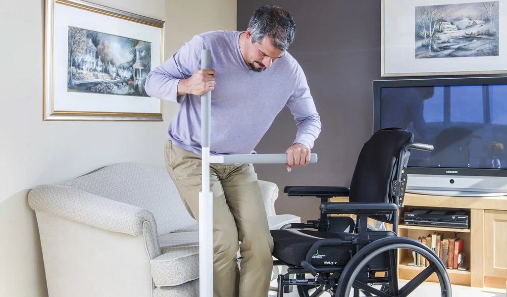 Man half standing with both hands on the grip and bar, mid transfer from armchair to wheelchair