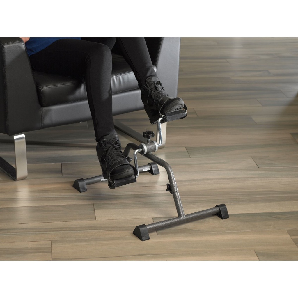 Person seated in a dark armchair pedalling the exercise peddler on a wood floor
