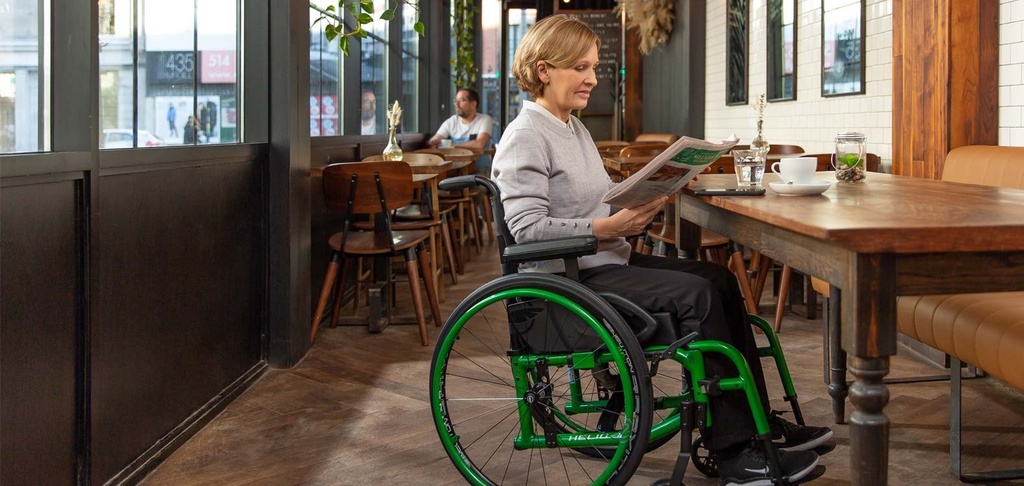 Woman reading at a cafe table while seated in a Helio A6 with a green frame