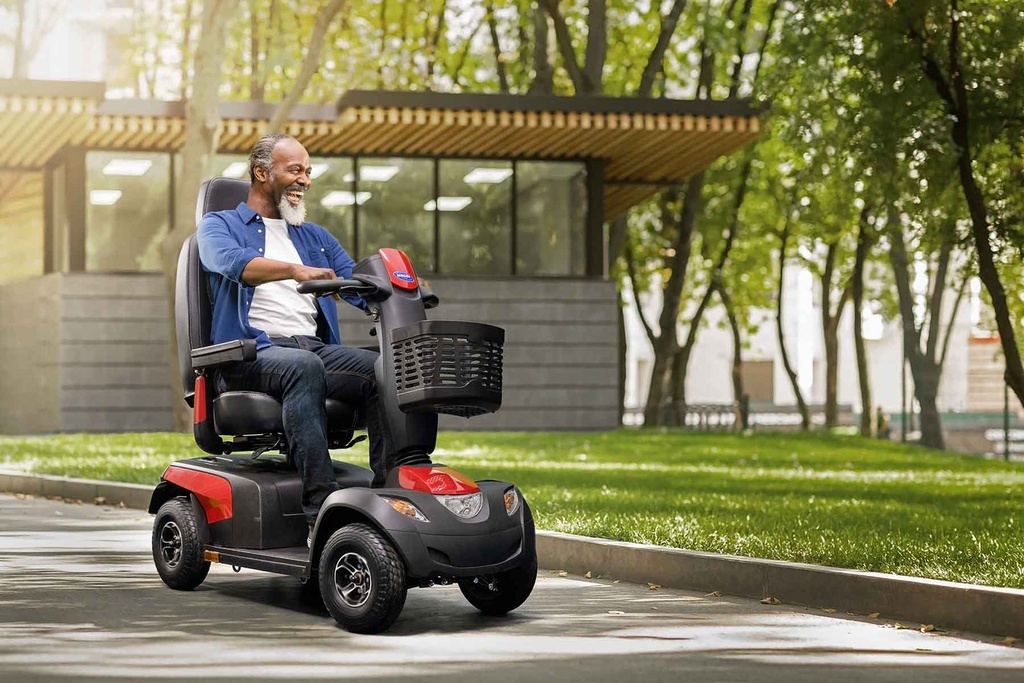 Man riding a red Comet Pro along a paved park path, front basket and headlight facing the camera
