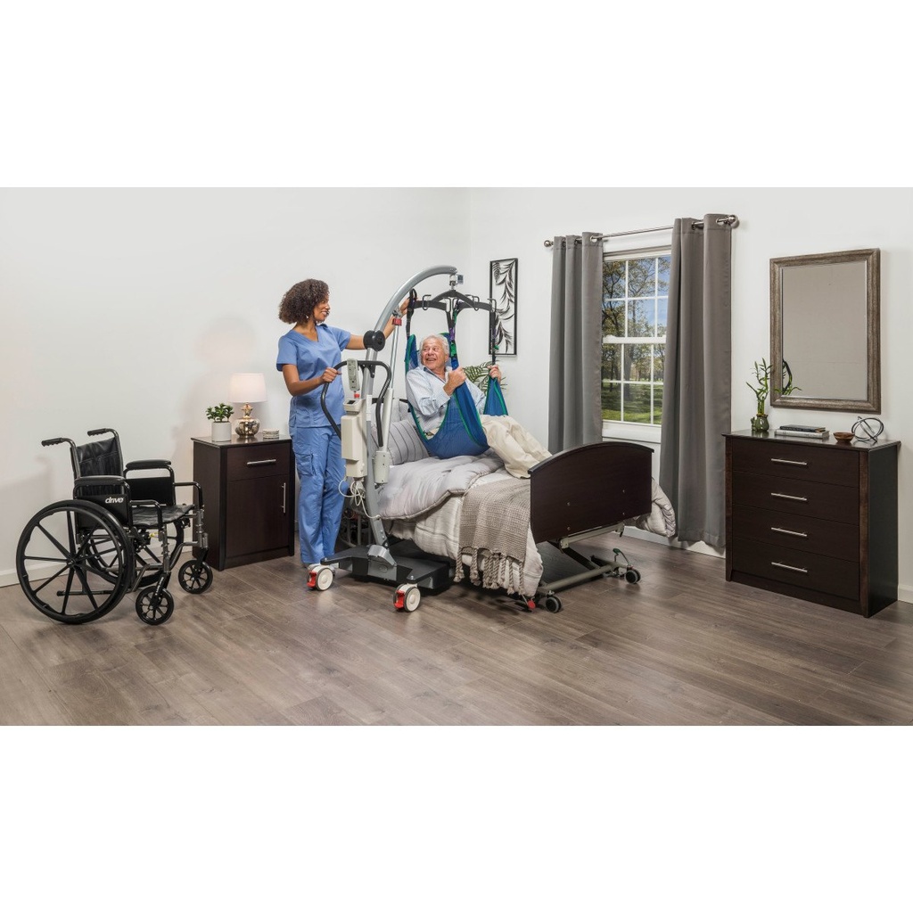 Caregiver using the Gravis patient lift beside a bed and wheelchair
