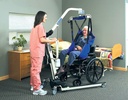 Caregiver raising a seated person in a blue sling with a Reliant floor lift beside a bed