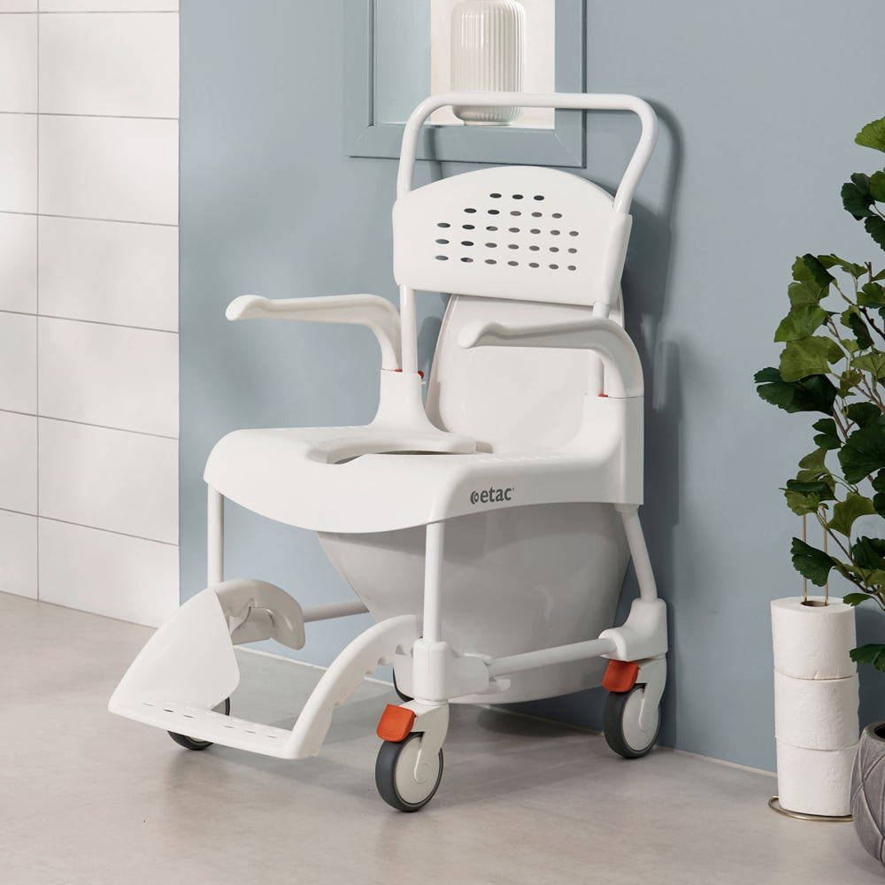 Etac Clean shower commode chair positioned over a wall-mounted toilet, showing the upright push handle