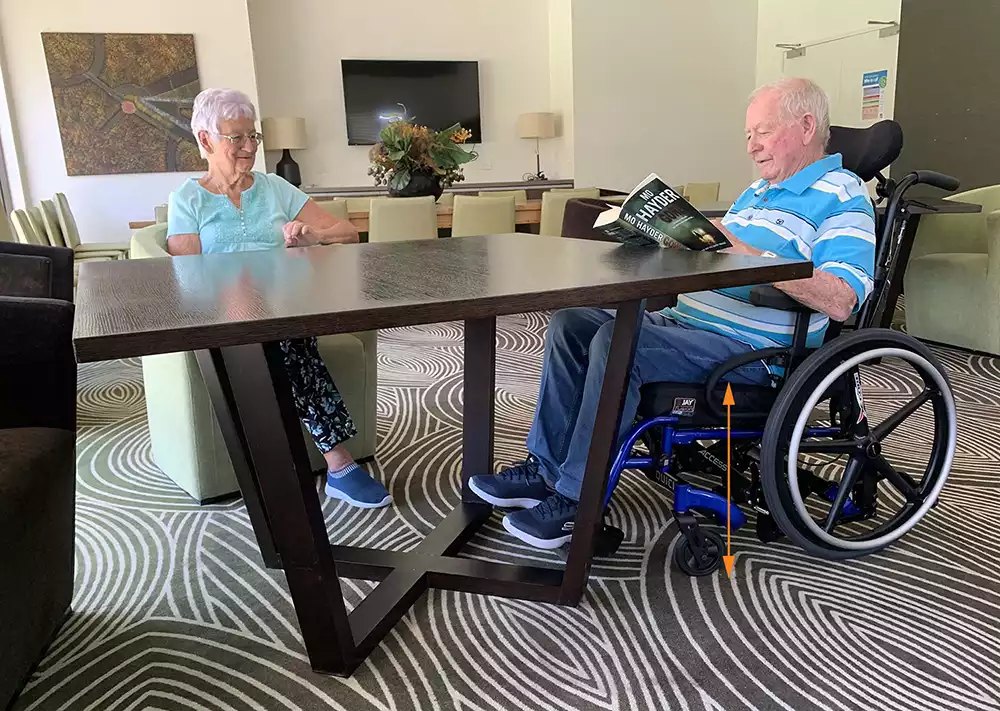 Man seated in a blue Quickie Access wheelchair pulled up to a table, showing the low seat height
