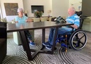 Man seated in a blue Quickie Access wheelchair pulled up to a table, showing the low seat height
