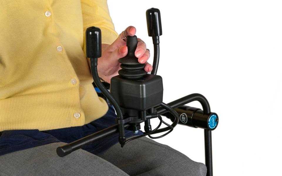 A hand gripping the VersaGuide EZ joystick on the chair, with a flex switch beside it