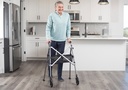 Person standing with a two-wheel walker and mesh basket in a kitchen