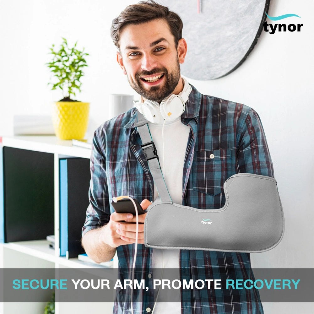 Man standing in an office holding a phone, wearing a Tynor Pouch Arm Sling