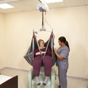Two caregivers with a seated person in a grey sling under a ceiling track