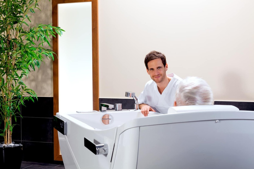 A carer beside a resident seated in the Beka Avero Motion E care tub