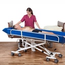A resident lying on the Sina Comfort trolley beside a bed while a carer stands over him