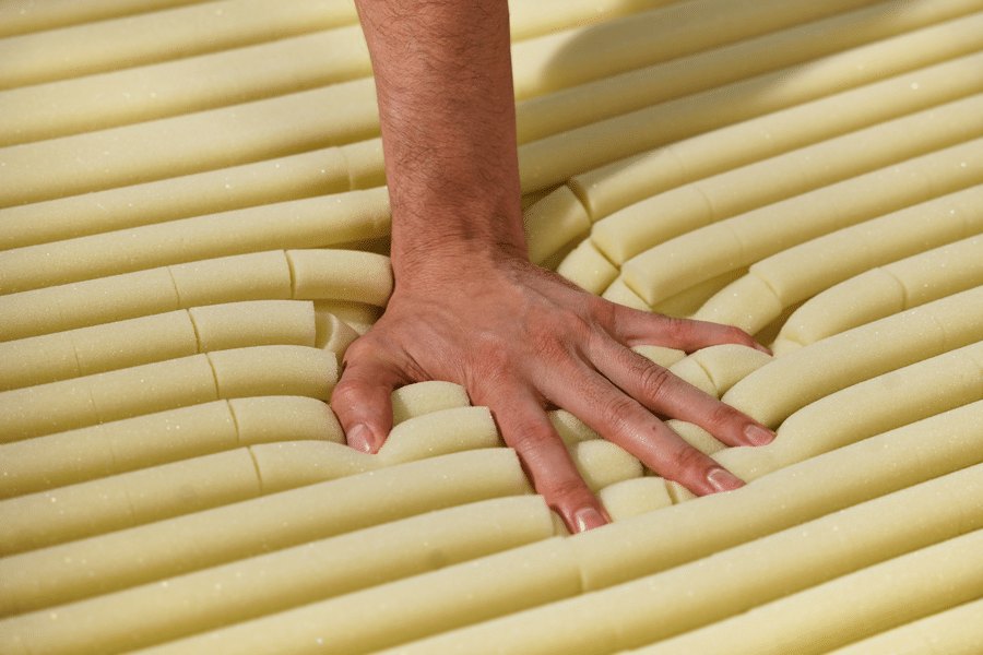 Close view of yellow foam tubes, a hand pressing the mattress surface.