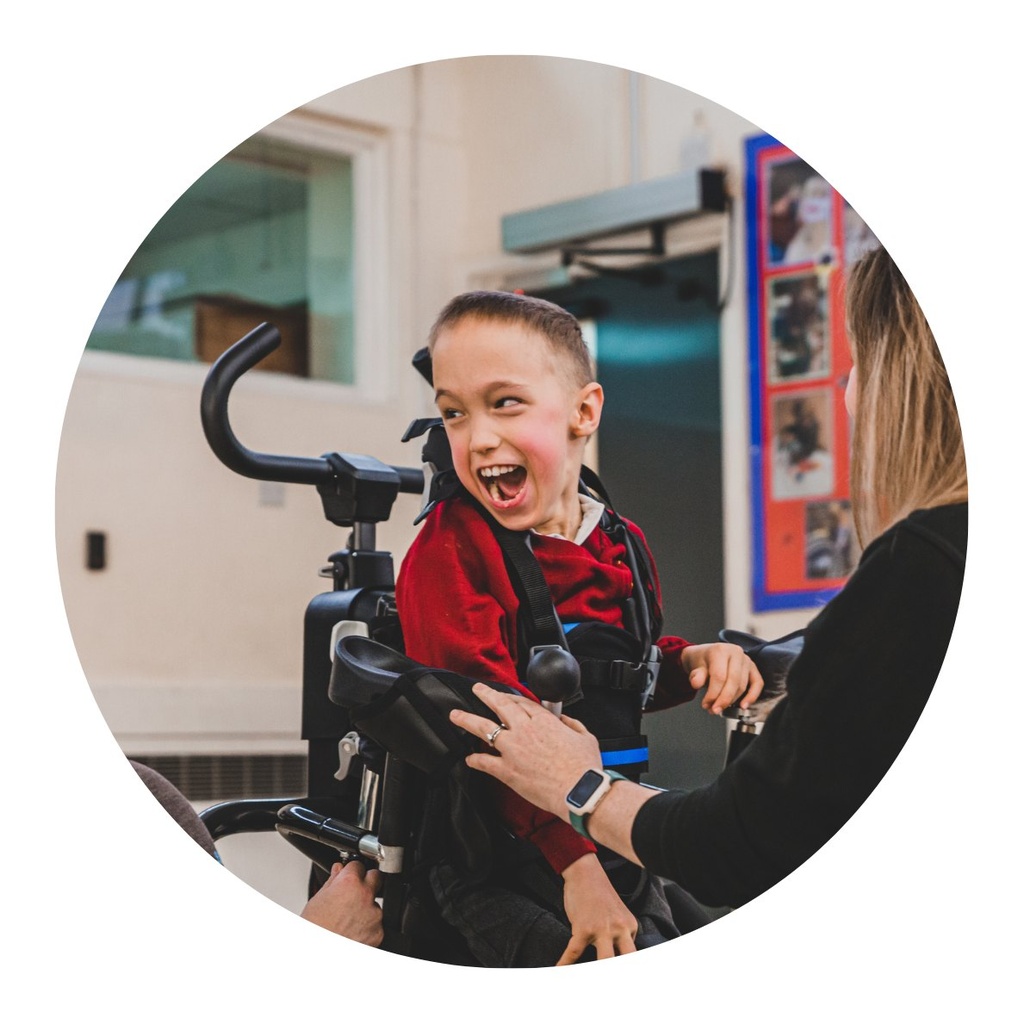 Child supported in the MyWay Plus harness indoors, with a therapist assisting