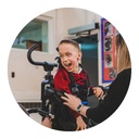 Child supported in the MyWay Plus harness indoors, with a therapist assisting