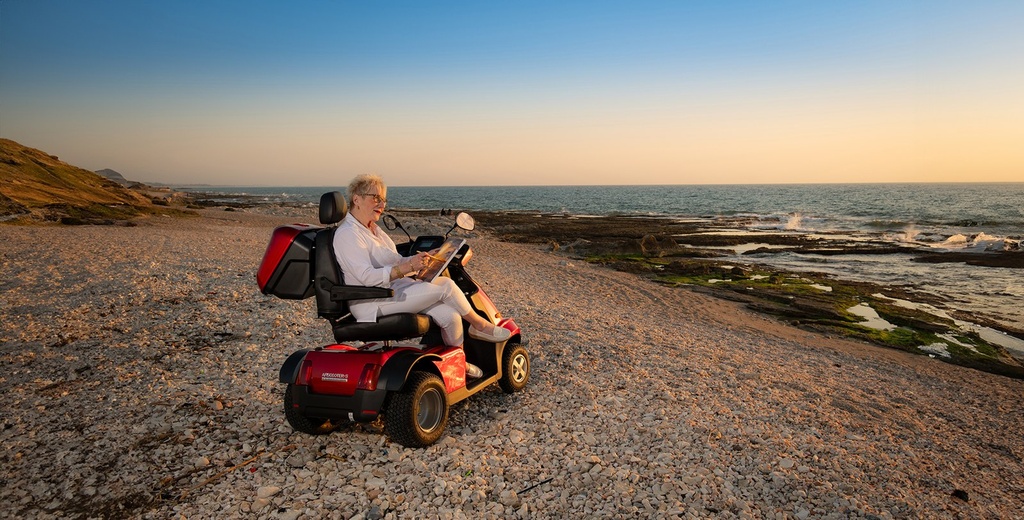 Woman sitting on a red Afiscooter S4 four-wheel scooter on a stony beach