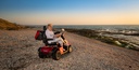 Woman sitting on a red Afiscooter S4 four-wheel scooter on a stony beach
