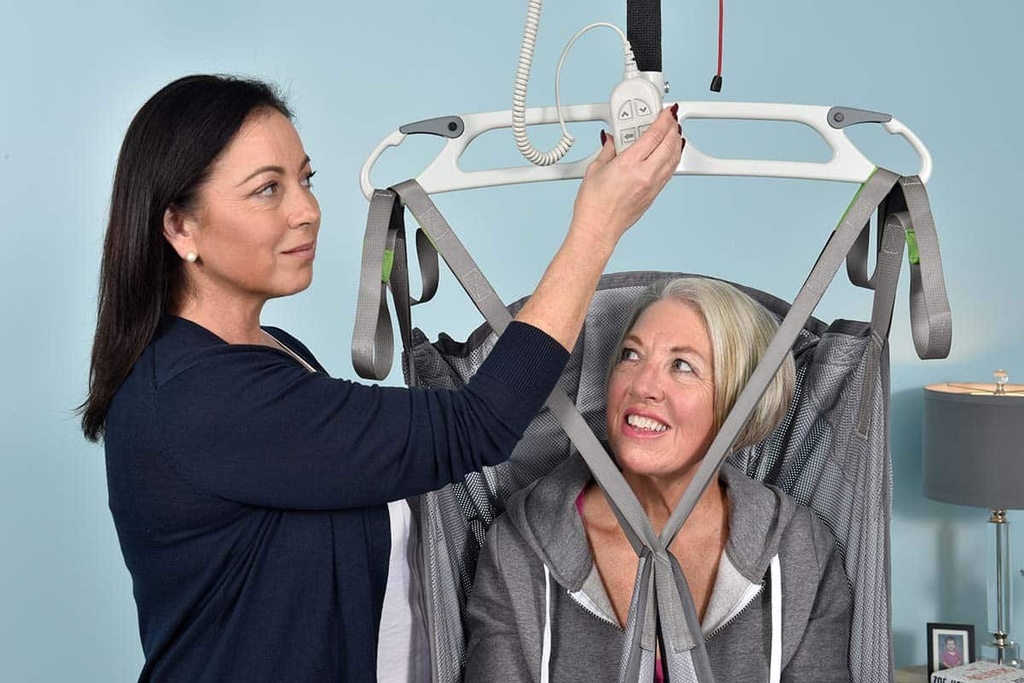 Carer holding the FL lift hand control while a person sits in a sling below the carry bar