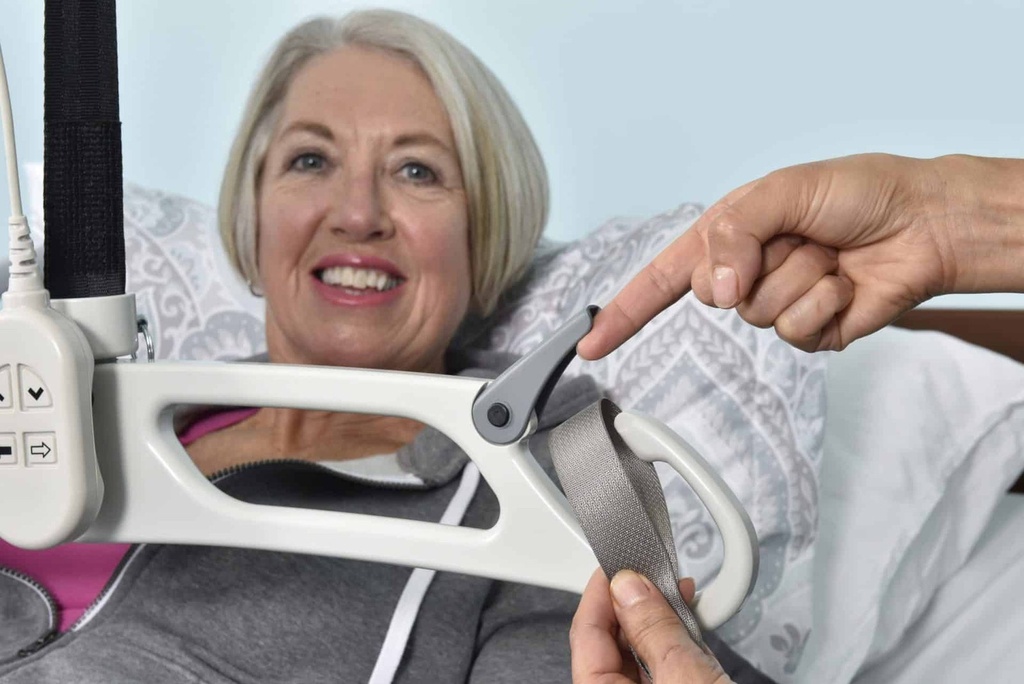 Carer clicking a sling strap into the FL lift carry bar safety latch above a person in bed