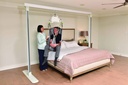 Monarch portable ceiling lift hanging from the Savaria Gantry beside a bed