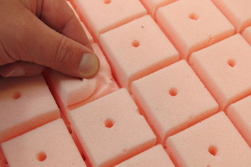 Fingers pressing a pink tear-off foam cube on the Comfi back's contoured surface
