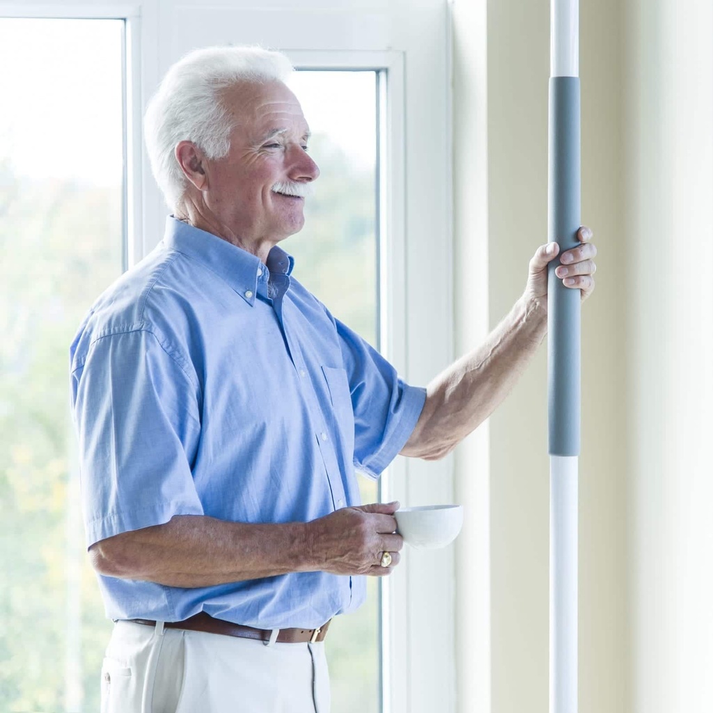 Older man steadying himself on the pole's grip by a window while holding a coffee cup